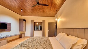 A bedroom with a bed, a ceiling fan, a TV mounted on the wall, and a door leading to another room.