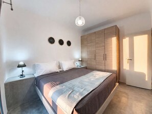 Un dormitorio con cama, mesitas de noche, armario y lámpara colgante.