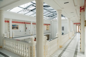 A spacious hotel lobby with a high ceiling, large columns, a glass skylight, and a checkered floor pattern. - Kampoeng Indonesia Hotel (Khoja Ismail)