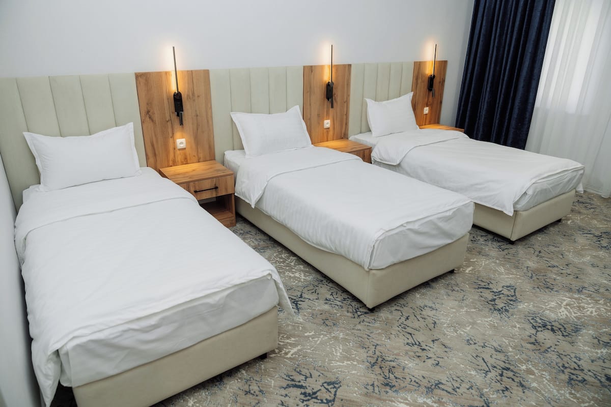 A hotel room with three beds, wooden headboards, bedside lamps, and a marble floor.