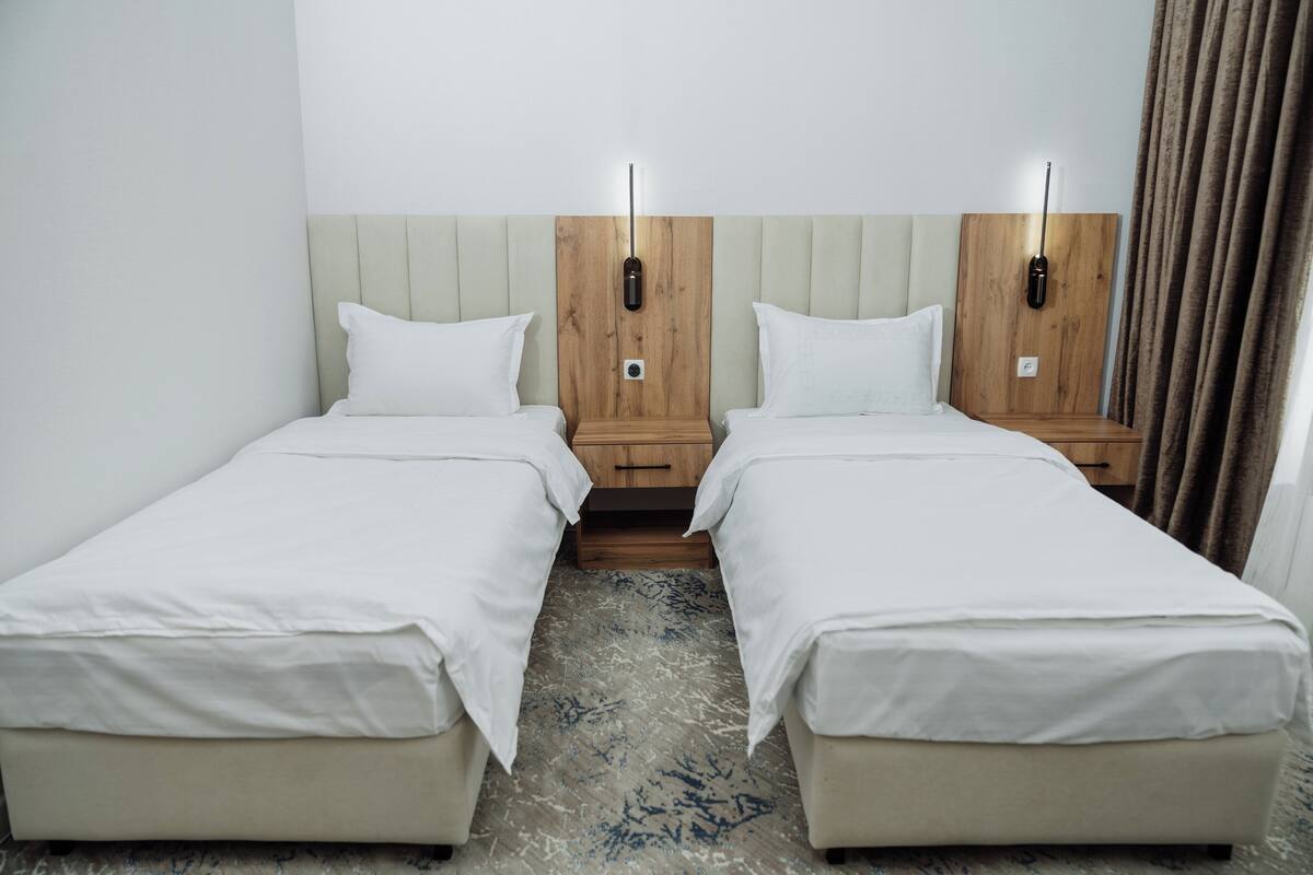 A hotel room with two single beds, wooden headboards, bedside tables, and a patterned carpet.