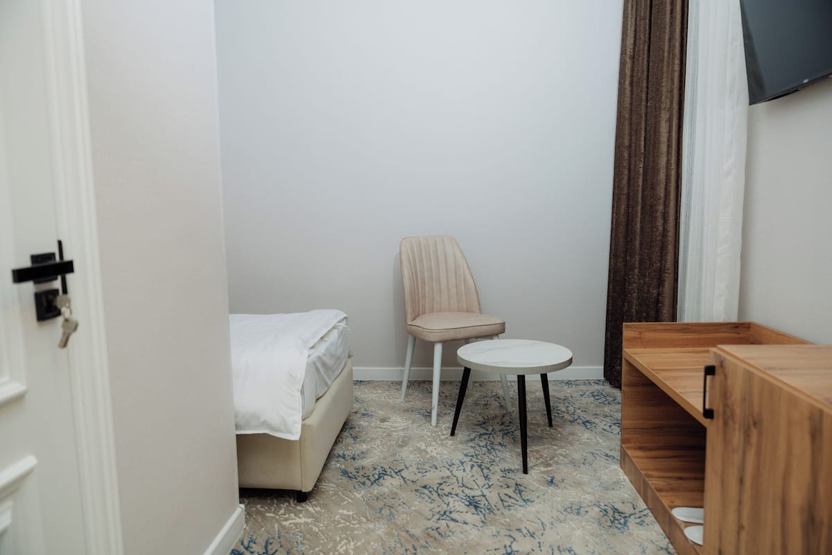 A small, neatly arranged room with a bed, a chair, a small table, and a wooden cabinet.