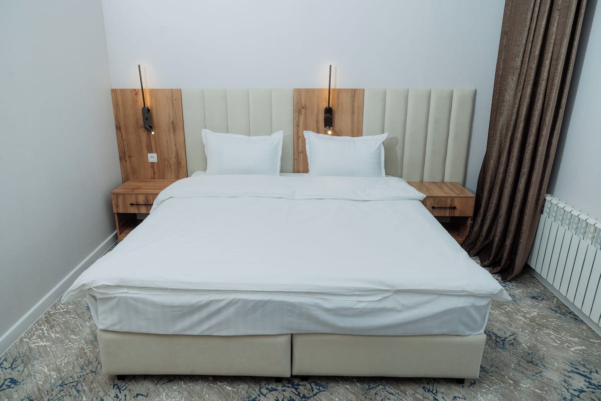 A double bed with a wooden headboard, two bedside tables, and a nightstand with a lamp.
