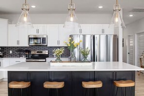 A modern kitchen with white cabinets, stainless steel appliances, and a central island with bar stools. - Relax @Lemon Twist! Lake views, Spacious 8BR, Theater, Arcades, Hot tub, Pools (Branson)