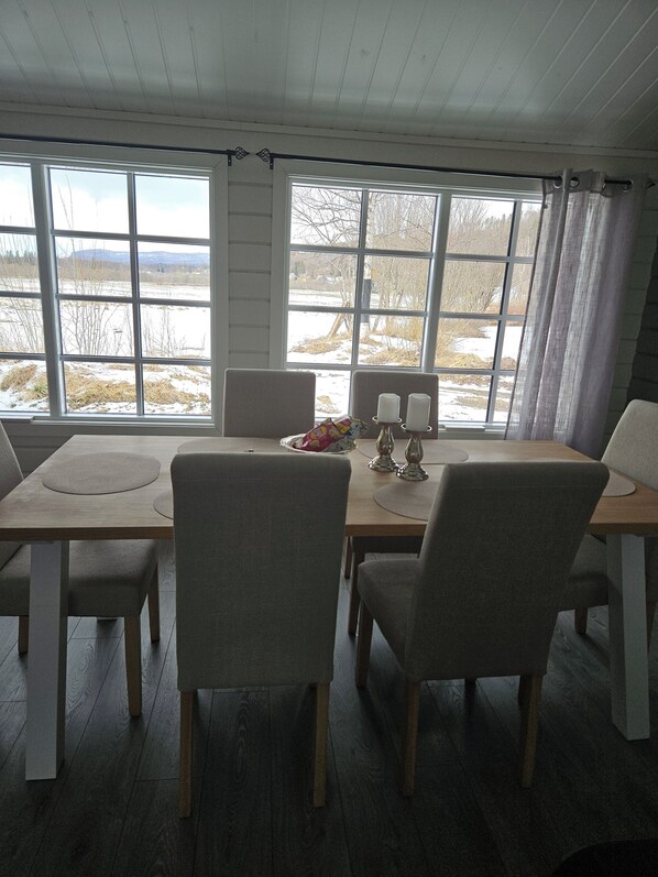A dining area with a table and chairs, a window with a view of a snowy landscape, and a candle holder on the table.