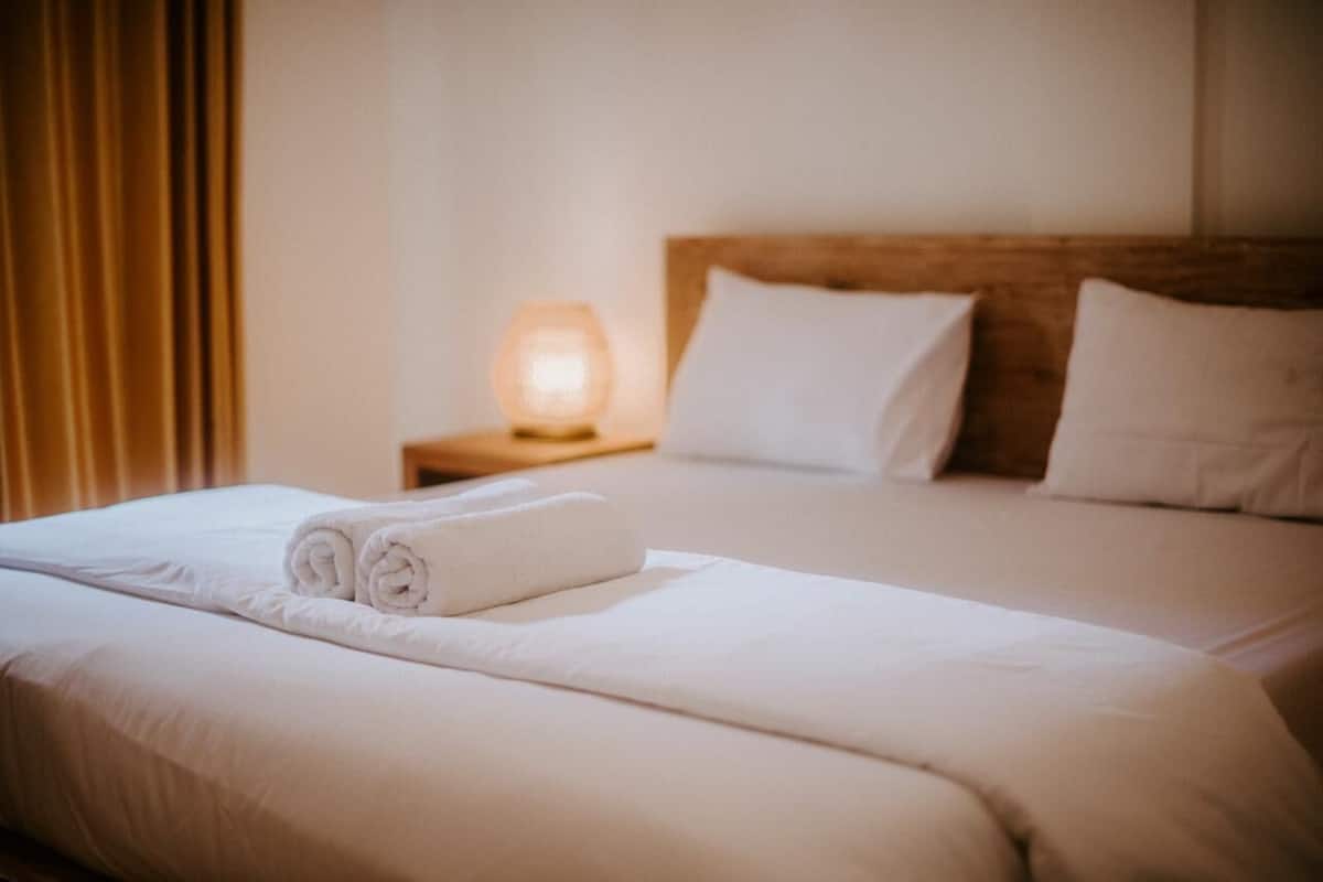 A neatly made bed with white linens, a wooden headboard, and a bedside lamp.
