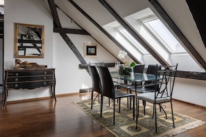 Ein Essbereich mit einem Glastisch, schwarzen Stühlen, einem gemusterten Teppich, einer Holzkommode und einem Bild an der Wand.