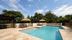Une piscine rectangulaire entourée d’une terrasse carrelée, agrémentée de deux parasols et de chaises longues.