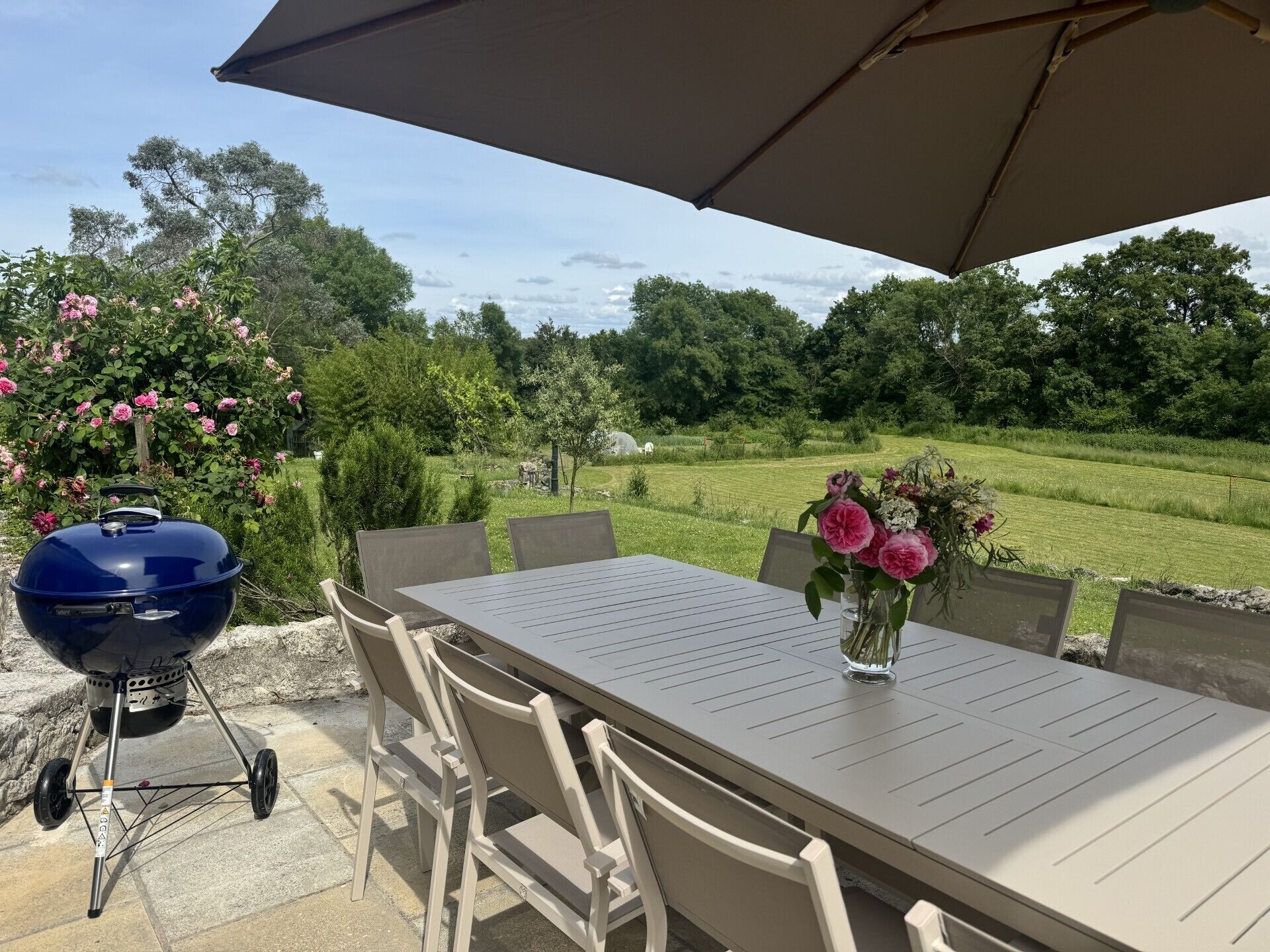 Un patio al aire libre con una mesa, sillas, una parrilla y un gran paraguas.