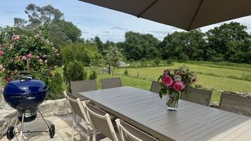 Un patio al aire libre con una mesa, sillas, una parrilla y un gran paraguas.