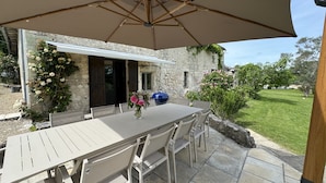 Une terrasse extérieure avec une table et des chaises, un barbecue et un grand parasol.