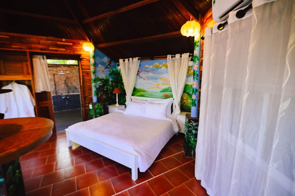 Une chambre à coucher avec un lit, des rideaux, une table de chevet, une table et une fresque murale.