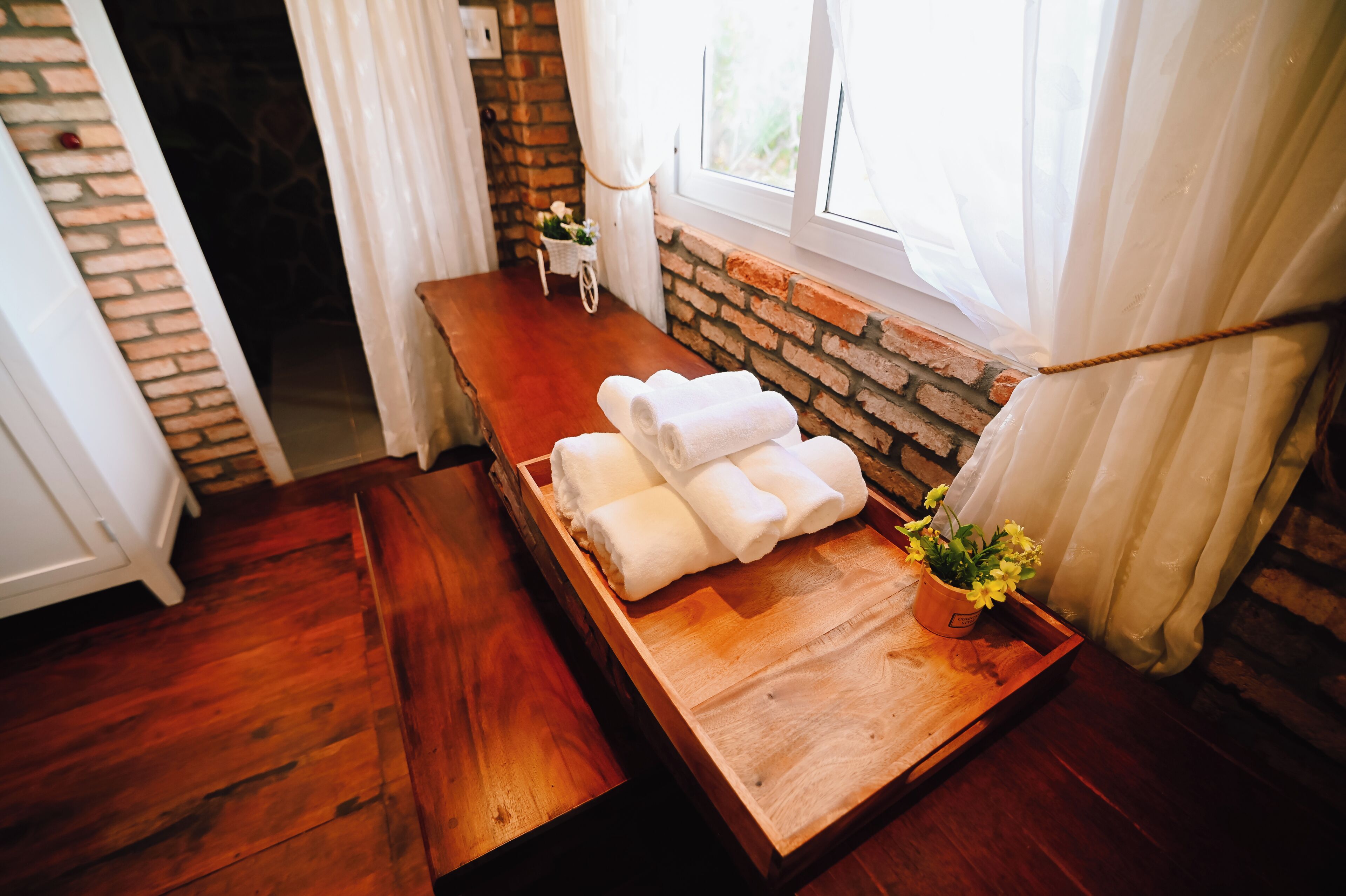 A wooden bench with a tray of folded towels and a potted plant.