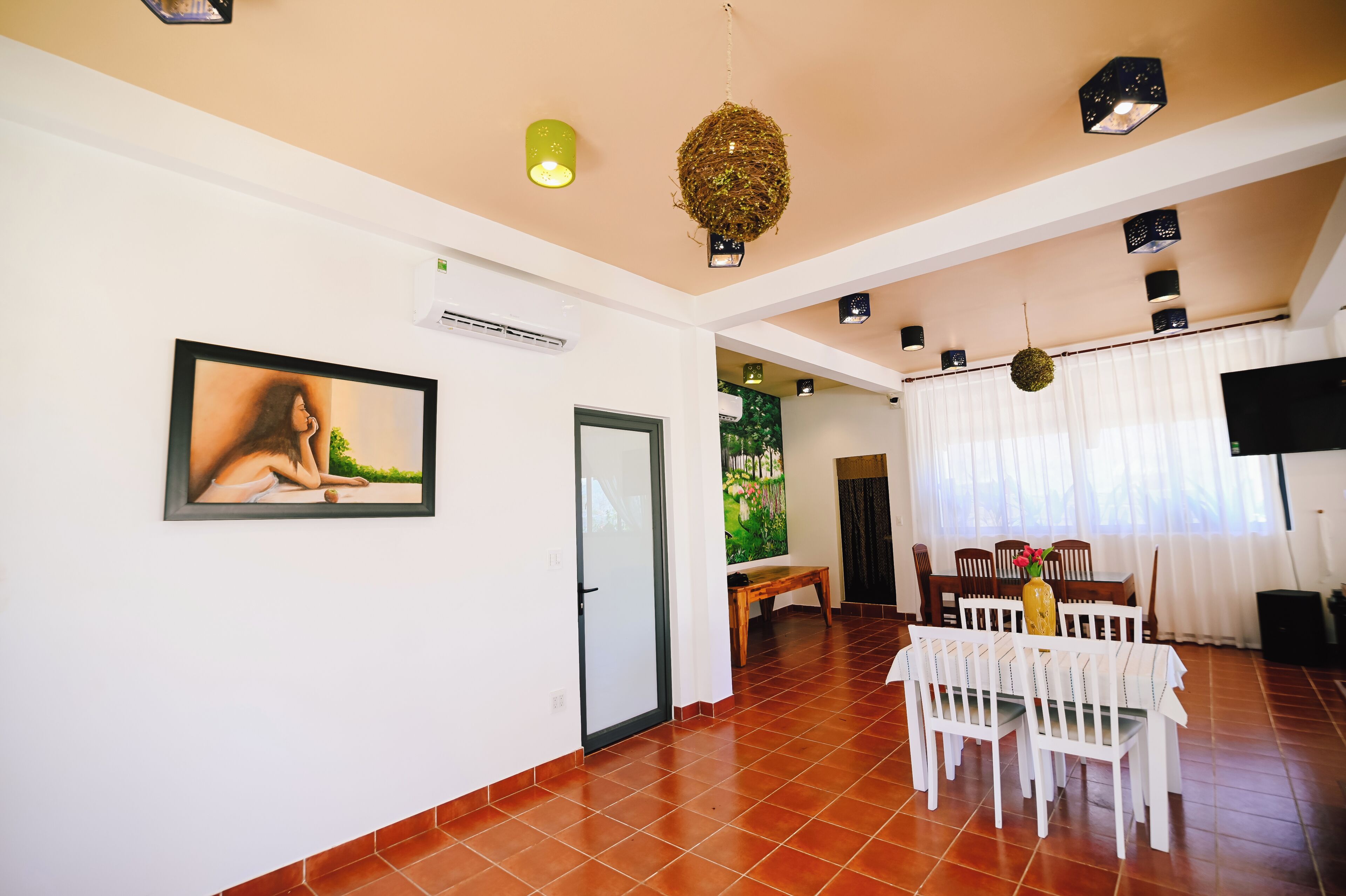 A spacious room with a dining area, a painting on the wall, and a ceiling with decorative lighting fixtures.