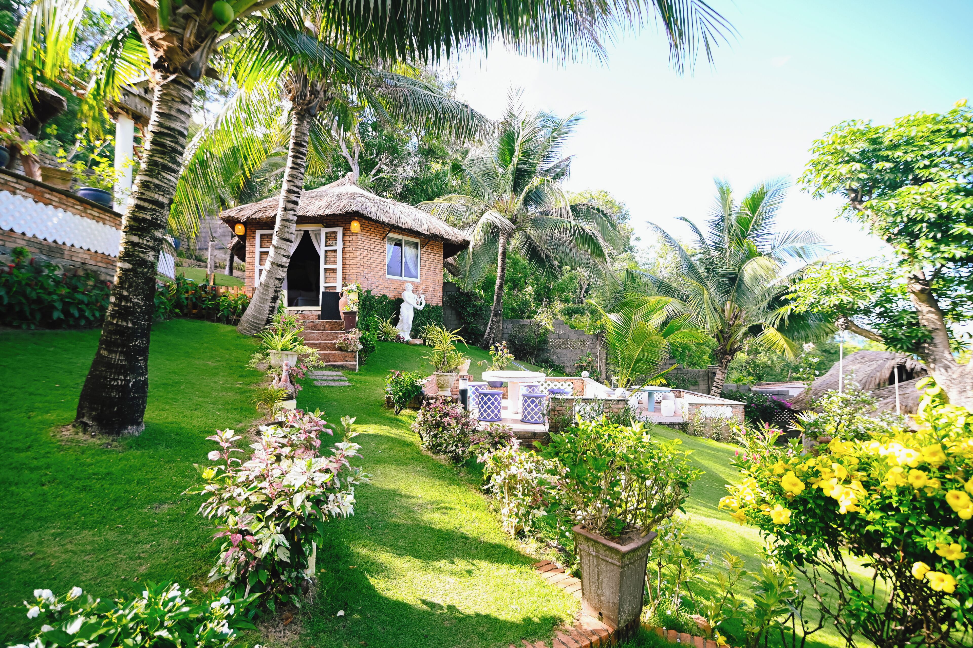 A thatched-roof house surrounded by lush greenery and palm trees.