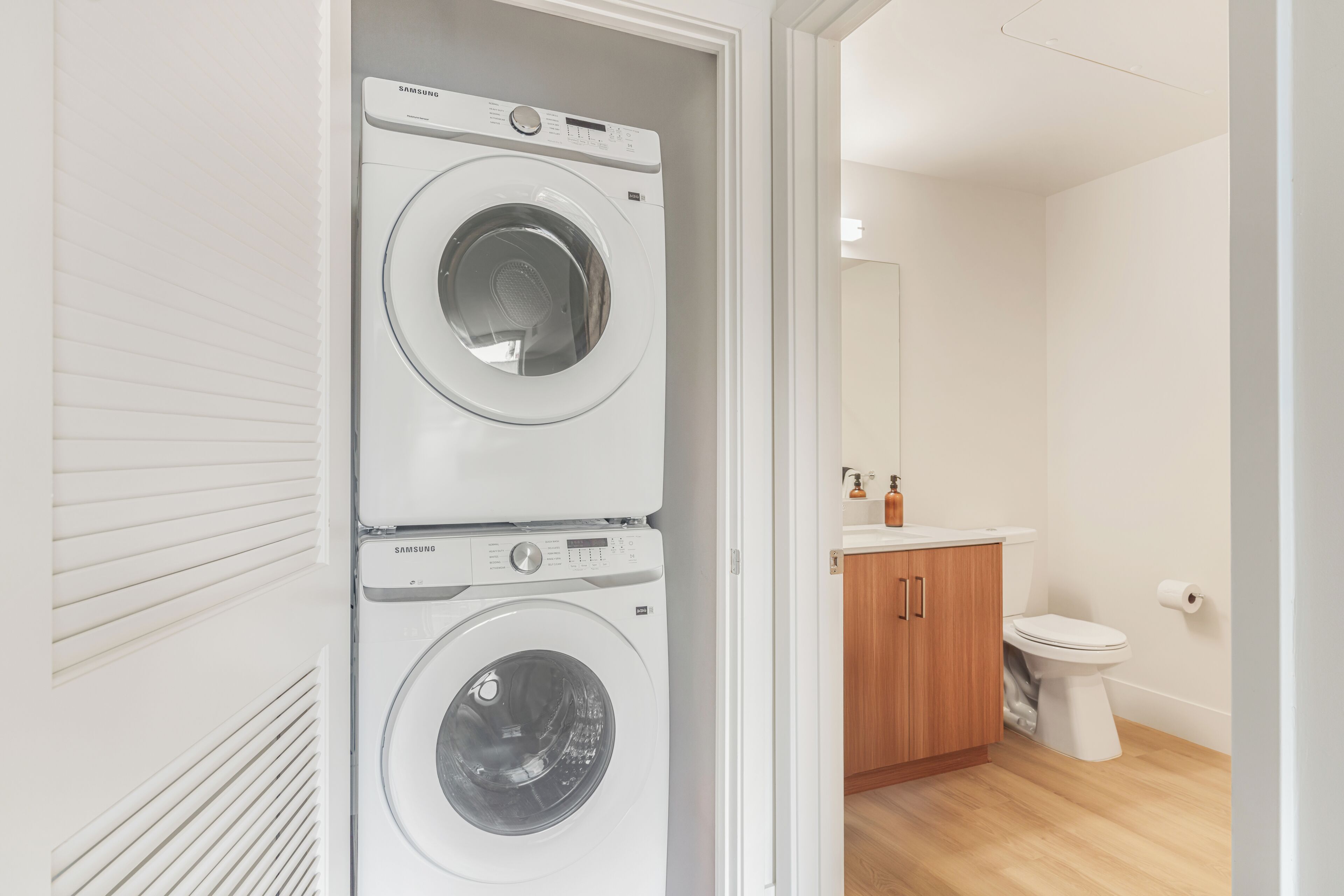 A laundry room with two Samsung washing machines, a toilet, and a wooden cabinet.