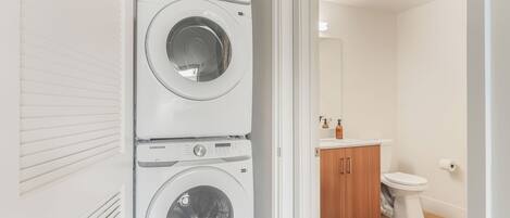 A laundry room with two Samsung washing machines, a toilet, and a wooden cabinet.