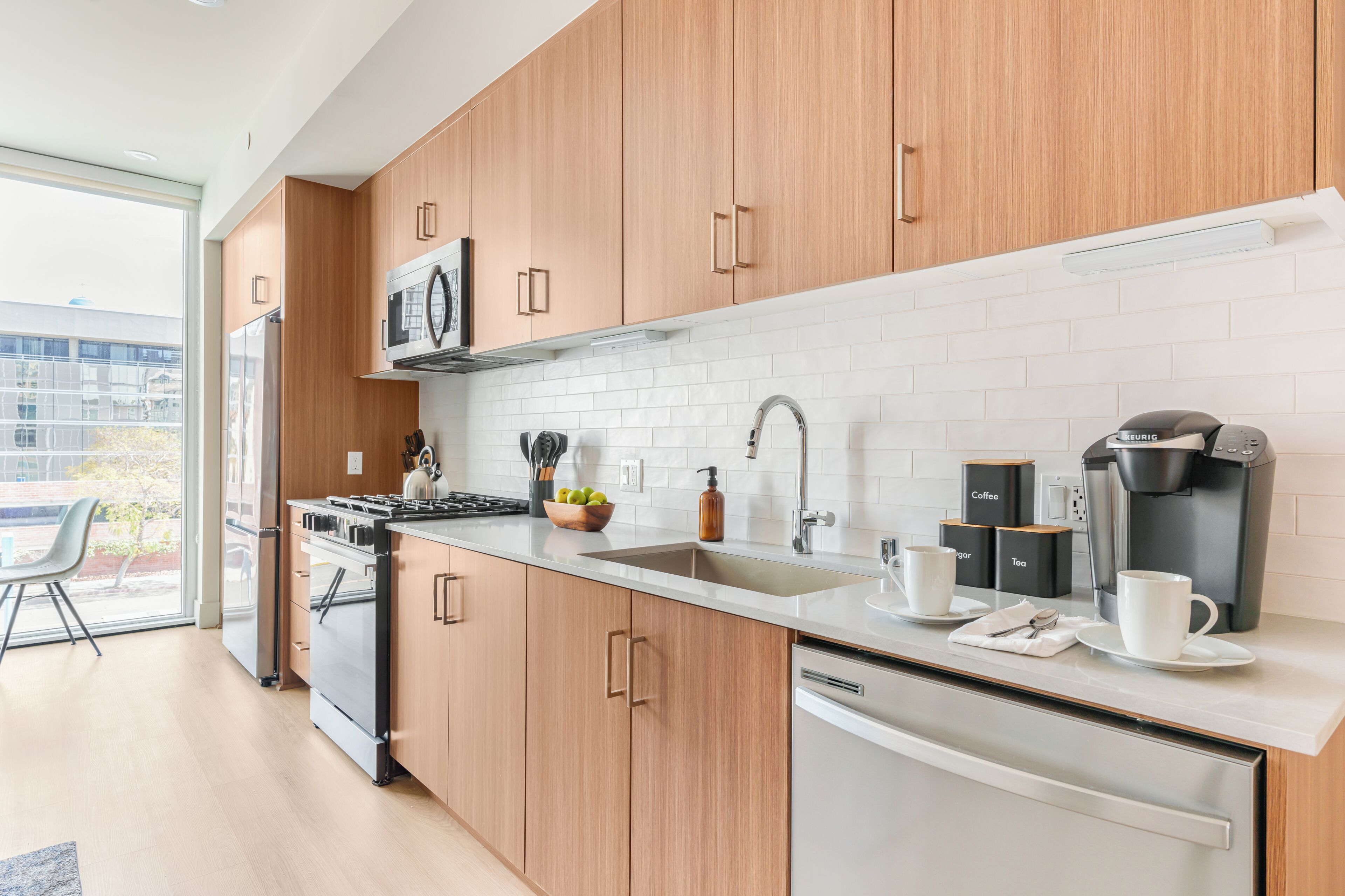 Una cocina moderna con armarios de madera, un lavamanos de acero inoxidable, una cafetera y un lavavajillas.