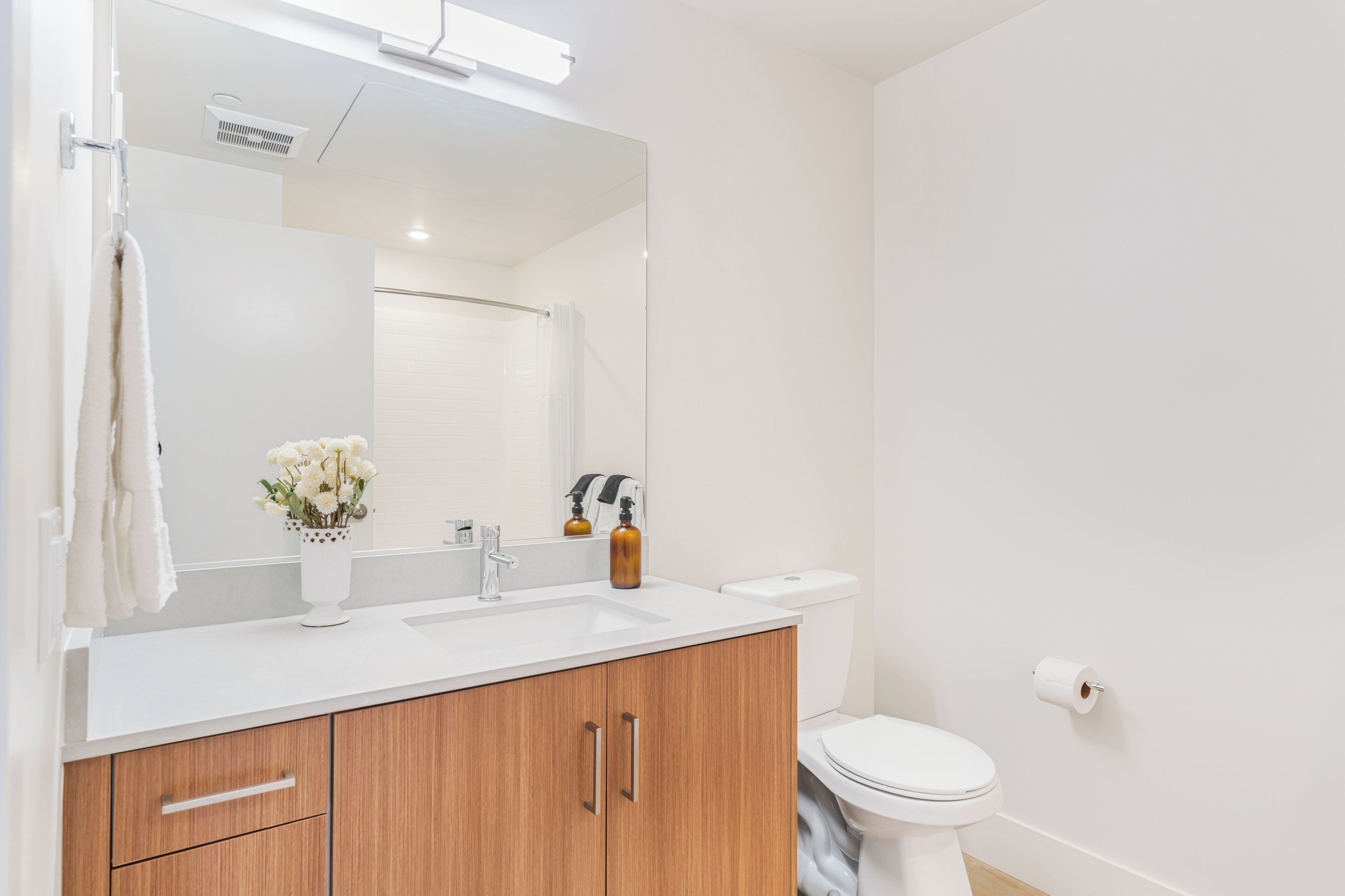 A modern bathroom with a white sink, wooden cabinets, a mirror, a toilet, and a towel rack.
