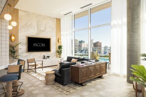 A modern living room with a large TV, comfortable seating, a dining area, and a view of a cityscape. - Gym + Rooftop Deck + Pool + Spa | Little Italy Locale | Ancora by AvantStay (San Diego)