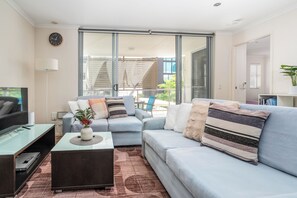 A modern living room with a sofa, a coffee table, a TV, and a sliding glass door leading to a balcony. - Merivale stay in South Brisbane two beds two baths one parking (South Brisbane)