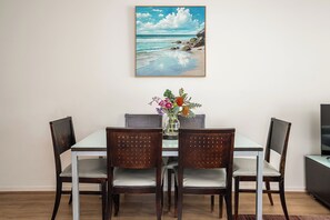 Ein Essbereich mit Tisch, vier Stühlen, einer Blumenvase und einem Gemälde mit Strandmotiv an der Wand.