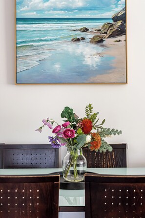 A framed painting of a beach scene above a dining table with a vase of flowers. - Merivale stay in South Brisbane two beds two baths one parking (South Brisbane)