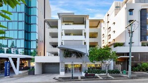 Un hôtel moderne doté d’une façade en verre, de nombreux balcons et d’une cour intérieure aménagée avec des sièges.