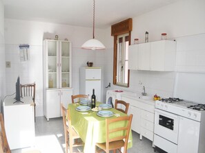 A compact kitchen with a dining table, chairs, a refrigerator, a stove, and a washing machine. - Casa vacanze Sakura a 230 metri dalla spiaggia Li Marangi di San Foca (San Foca)