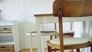 Ein Zimmer mit Holzboden, einem weißen Stuhl mit Sitzgeflecht und einem weißen Tisch mit einer gewobenen Tischdecke.