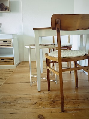 A room with wooden flooring, a white chair with a woven seat, and a white table with a woven tablecloth. - Studio "Wolfi" for 1 - 2 persons, all-in-one, super cozy, pets welcome (Pähl)
