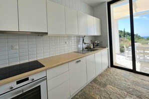 A modern kitchen with white cabinets, a wooden countertop, and a view of the outdoors through a large window. - Villa Porto Mella in Vasilikos, Zakynthos (Zakinthos)
