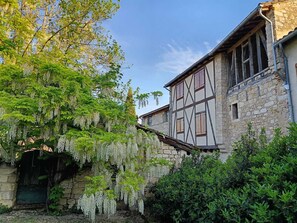 Un bâtiment traditionnel en pierre, doté d’une structure en bois apparent, d’une arche en pierre et d’une végétation luxuriante.