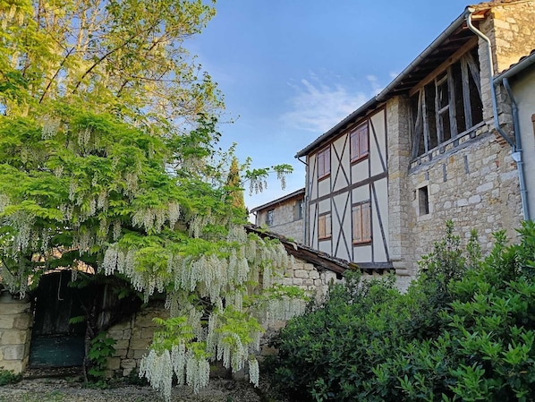 A traditional stone building with a timber-framed structure, a stone archway, and lush greenery.