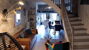 A spacious living area with a staircase, a dining area, and a kitchen visible through an archway. - Charming 13th-century house in a medieval village in the heart of the Golden Triangle (Cestayrols)