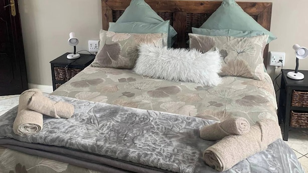 A neatly made bed with a floral-patterned bedspread, two pillows, and a fluffy white throw. - Rustic Red Serene & Comfortable Country Home (Benoni)