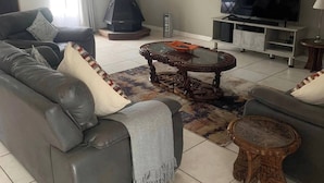 A living room with a sofa, TV, fireplace, and a clock on the wall. - Rustic Red Serene & Comfortable Country Home (Benoni)