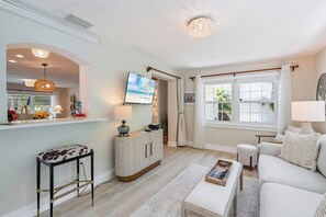 A living room with a sofa, a coffee table, a TV, and a window with curtains. - Island Charm (Holmes Beach)
