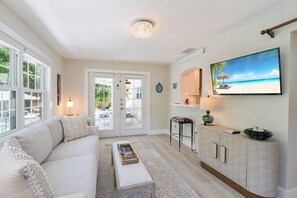 Ett vardagsrum med en soffa, ett soffbord, en tv och en matplats med en bardisk.