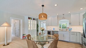 Une cuisine moderne avec des meubles blancs, une table à manger en verre, des chaises en osier et un luminaire suspendu.