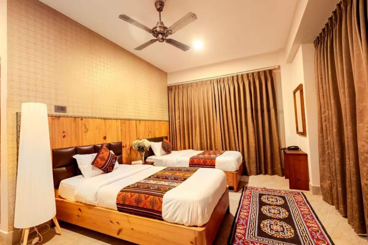 A hotel room with two beds, a ceiling fan, a wooden headboard, a patterned rug, and a large window with curtains.