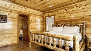 Interior de uma cabana de madeira com cama, paredes de madeira e ventoinha no teto.