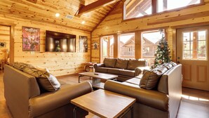 Interior de cabana de tronco com teto de madeira, sofás de couro, mesa de madeira e árvore de Natal.
