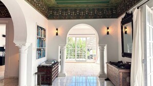 Un pasillo amplio con suelo de mármol, una estantería, un mueble decorativo y un gran ventanal de arco.
