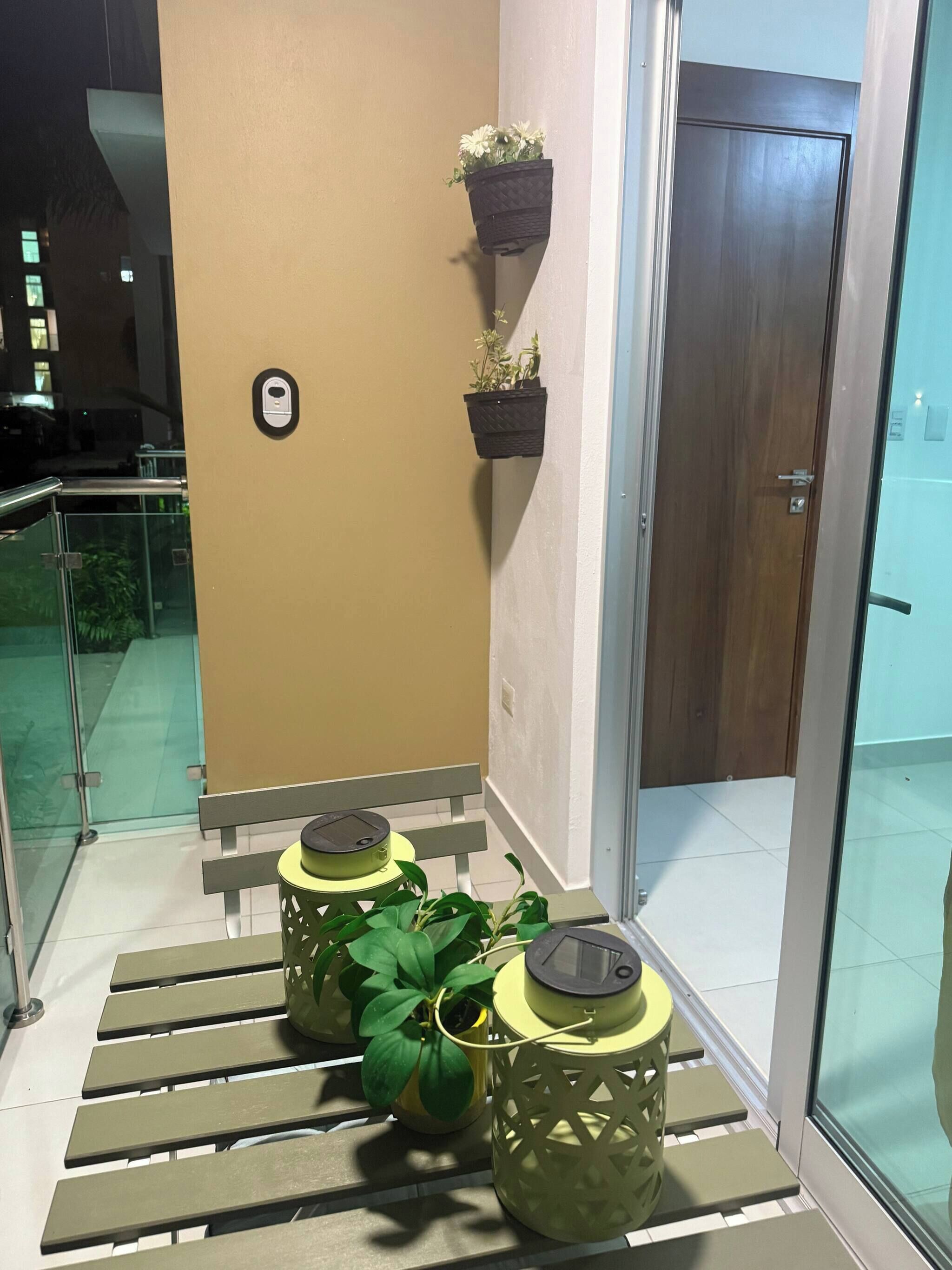 Un rincón de una habitación con un banco, una planta en maceta, un jarrón de pared y una puerta.