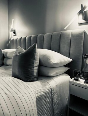 A bed with a striped bedspread, multiple pillows, a nightstand with a lamp, and a wall-mounted light fixture.