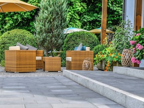 Terrassenmöbel aus Rattan mit Kissen, ein kleiner Baum und ein Blumentopf mit Blumen.