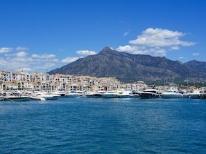 Ein Yachthafen mit vertäuten Booten, eine Küstenstadt mit weißen Gebäuden und ein Berg im Hintergrund.