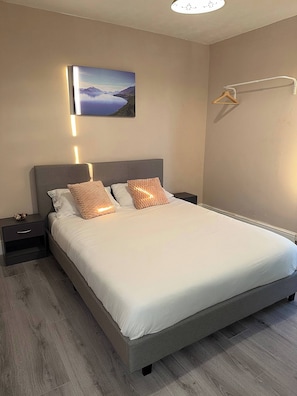 A modern bedroom with a large bed, two bedside tables, a wall-mounted light, and a picture of a landscape. - The Railway House, Colchester (Colchester)
