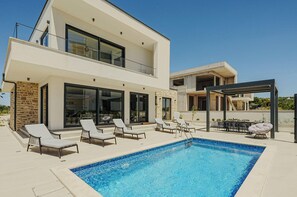 Une maison moderne à deux étages dotée d’une piscine, de chaises longues et d’un espace salon extérieur.